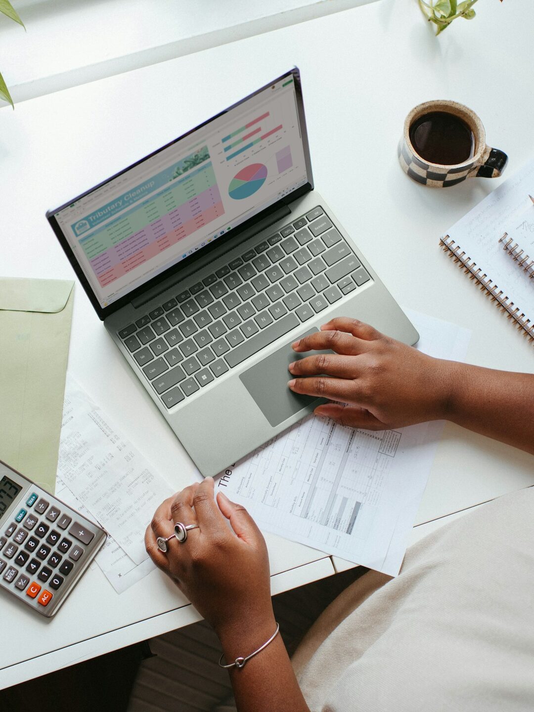 An overhead view of a desk with a laptop showing figures, a calculator and paperwork